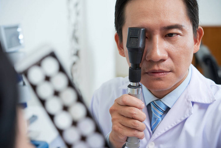 亚洲医生在白色医疗长袍中使用特殊工具检查医院病人视力