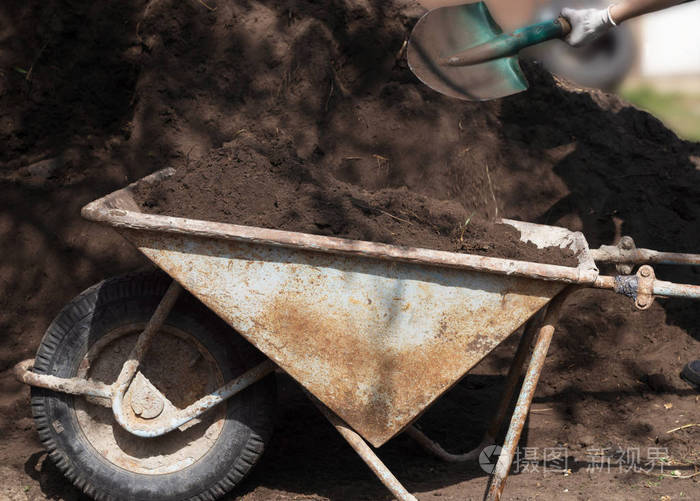 一个人用铲子把泥土倒在手推车里