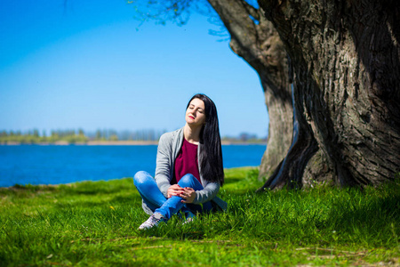 绿色阳光公园大树年轻性感的光脚女孩穿着白色短裙在大榕树上摆姿势.