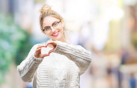 年轻美丽的金发女子戴着眼镜在孤独的背景微笑在爱显示心脏符号和形状用手。浪漫概念