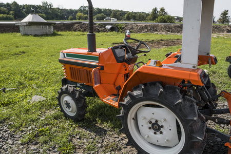 一个小的迷你橙色拖拉机站在农场院子上的绿草和等待工作开始