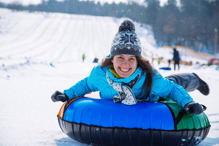 年轻的微笑的女孩乘坐雪橇雪管山冬季活动概念