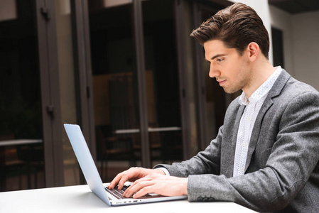 集中的年轻商人穿着西装在笔记本电脑上工作, 而坐在户外
