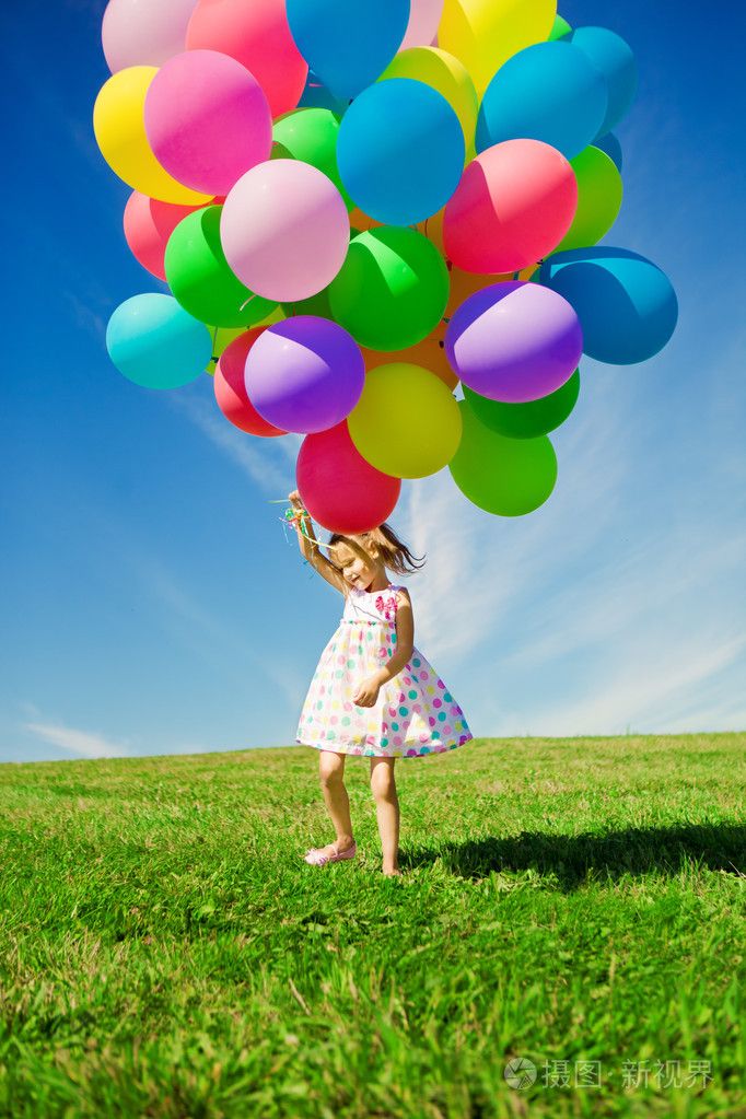 小女孩控股五颜六色的气球孩子在玩在一座绿色