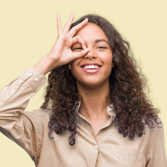 年轻的西班牙商界妇女做 ok 手势用手微笑, 眼睛看通过手指与愉快的