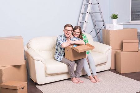 家, 搬迁和移动概念在眼镜愉快的夫妇持有卡板和坐在沙发上