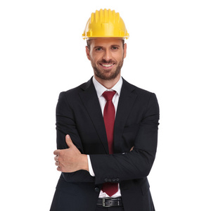自信的经理的肖像与黄色保护头盔站立在白色背景与武器折叠