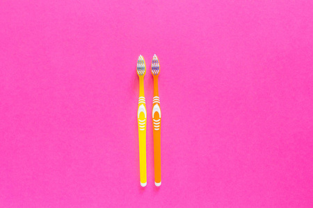 两个黄色和橙色的牙刷在明亮的粉红色背景特写。牙刷位于背景中间。复制空间