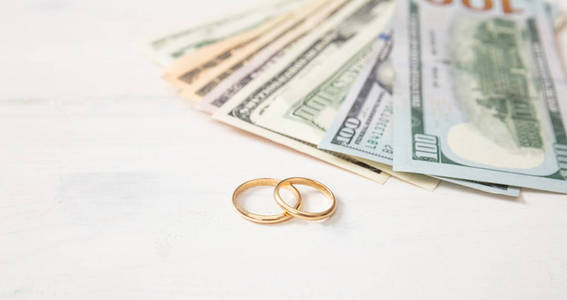 婚姻和开支概念。孤立的金色结婚戒指和美元, 在白色的木质背景, 复制空间