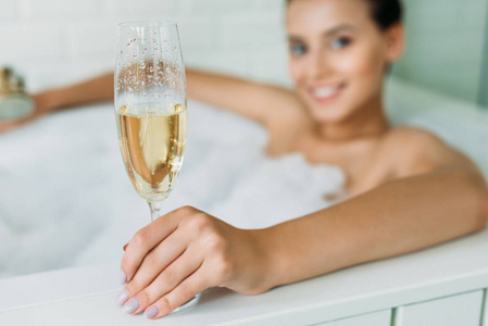 在浴缸里抱着香槟的美丽微笑的年轻女子特写视图