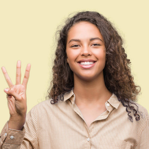 年轻的西班牙裔商业妇女显示和指向手指数三, 而微笑的信心和快乐