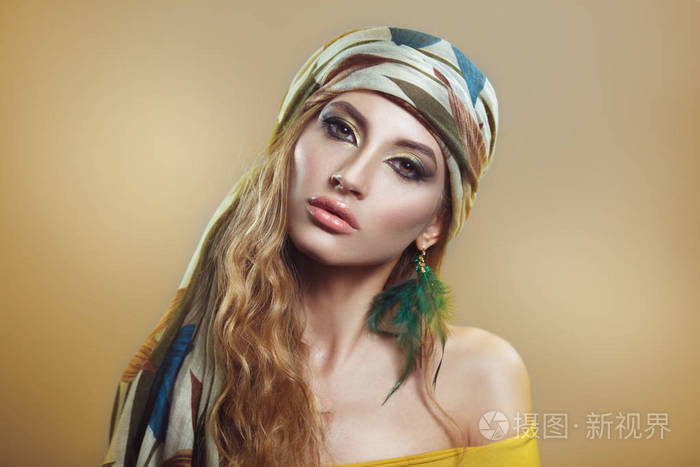 美丽的肖像在一个漂亮的女孩在围巾与明亮的金色阿拉伯化妆在米色背景