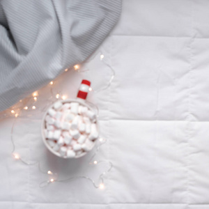新年或圣诞节平躺顶部视图与热可可咖啡巧克力与棉花糖杯圣诞节节日庆祝在床上与灯。模糊散焦方形背景