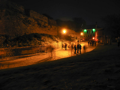 夜城市风景与步行的人。灯火通明的古代街道与铺路石
