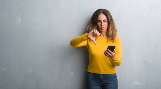 中年拉美裔妇女使用智能手机与愤怒的脸, 消极的迹象显示不喜欢拇指下降, 拒绝概念