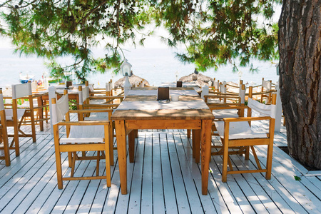 一个雪白的露台上有桌子的餐厅, 俯瞰着松树树枝下的大海