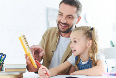 微笑的父亲和小女儿在家一起做家庭作业