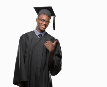 年轻毕业的非洲裔美国男子在孤立的背景微笑着快乐的脸看着, 并指向侧面与拇指向上