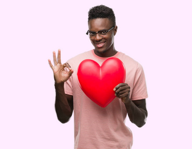 年轻的非洲裔美国人持有红色心脏做 ok 标志与手指, 优秀的标志