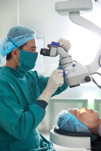 医生制服的亚洲医生人用手术显微镜探索成熟病人的眼睛