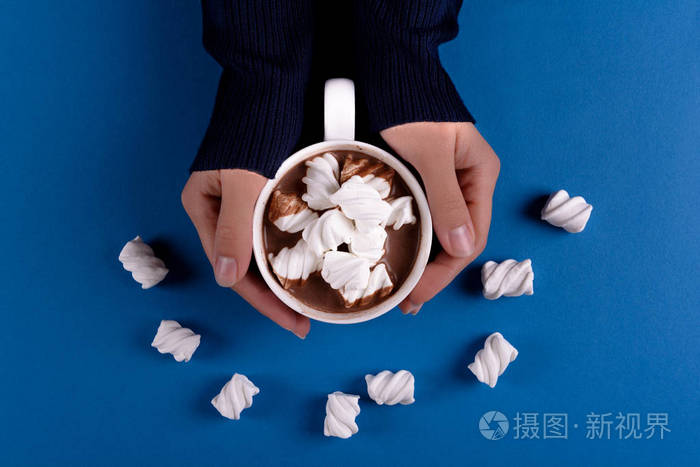 女性手拿着热巧克力与棉花糖糖果在蓝色纸背景顶部视图复制空间