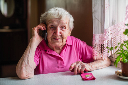 老年妇女坐在家里的一张桌子旁用手机交谈