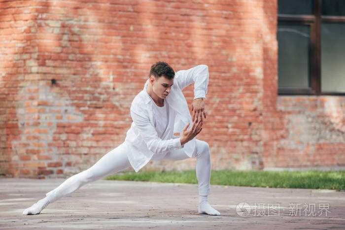 穿着白色衣服在街上练习的英俊的年轻男舞者