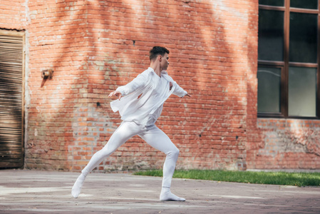 穿着白色衣服在街上练习的年轻男舞者