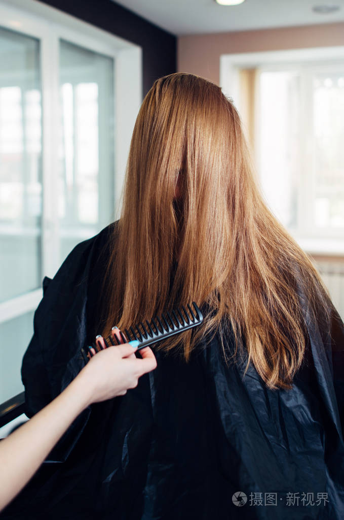 女性顾客的长直头发梳理出股当着她的面在美容院工作的一名理发师笑