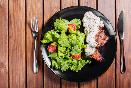 烤肉配新鲜蔬菜沙拉和西红柿, 黑色盘子, 木质背景。热鲜肉菜