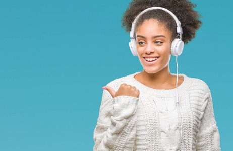 年轻的美国黑人妇女戴着耳机在孤立的背景下指向和显示与拇指到一边, 快乐的脸微笑