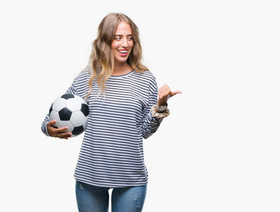 美丽的年轻金发碧眼的女人拿着足球在孤立的背景指向和显示与幸福的脸微笑的边