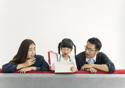 亚洲女儿与爸爸妈妈在客厅的沙发上打开礼物。概念家庭生日