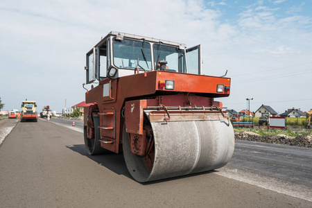 在沥青路面工程中进行道路修复的橙色重型振动压路机。在新的道路建设工地工作。修复