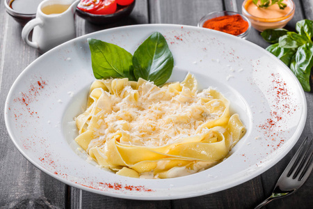 面条意大利面食与意大利干酪, 罗勒和奶油酱在黑暗的木质背景, 意式菜肴。餐桌上的配料