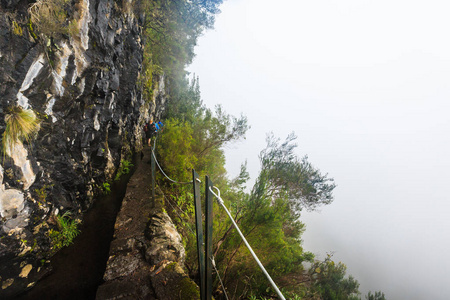 陡峭的深渊旁边的步行小径沿线的 levada 在山上的马德拉, 葡萄牙在雨天雾天
