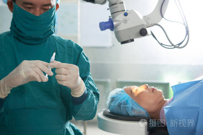 亚洲男子身着制服的外科医生准备注射注射器给躺在灯光下手术台上的