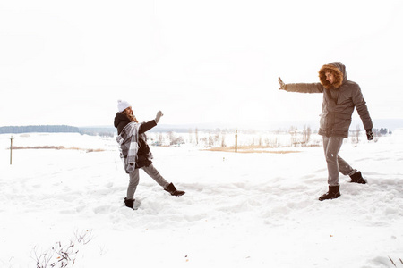 无忧无虑的愉快的年轻夫妇有乐趣一起在雪在冬天林地投掷雪球在对方在模拟战斗