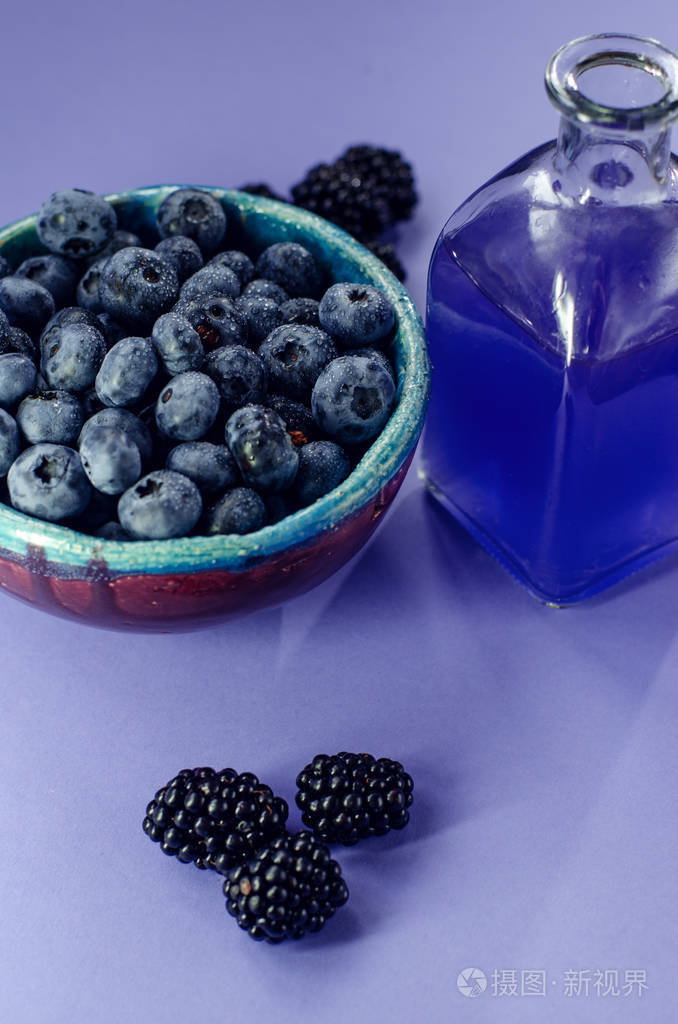 新鲜的浆果。蓝莓在一盘, 花, 黑莓与玻璃汁和树莓在蓝色背景