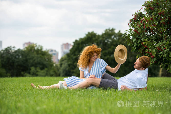 微笑红头发的女人试图把自己的草帽在男友的头上草地上公园