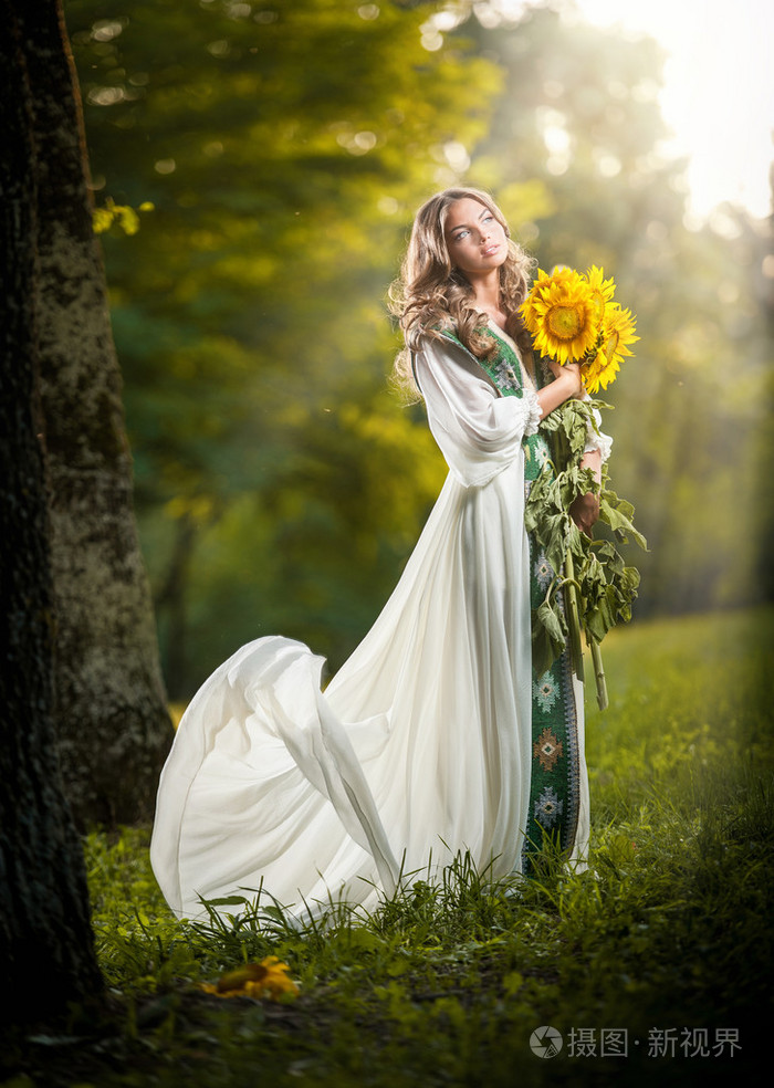 穿着一件持有向日葵户外拍摄的长长的白色裙子的年轻女子.