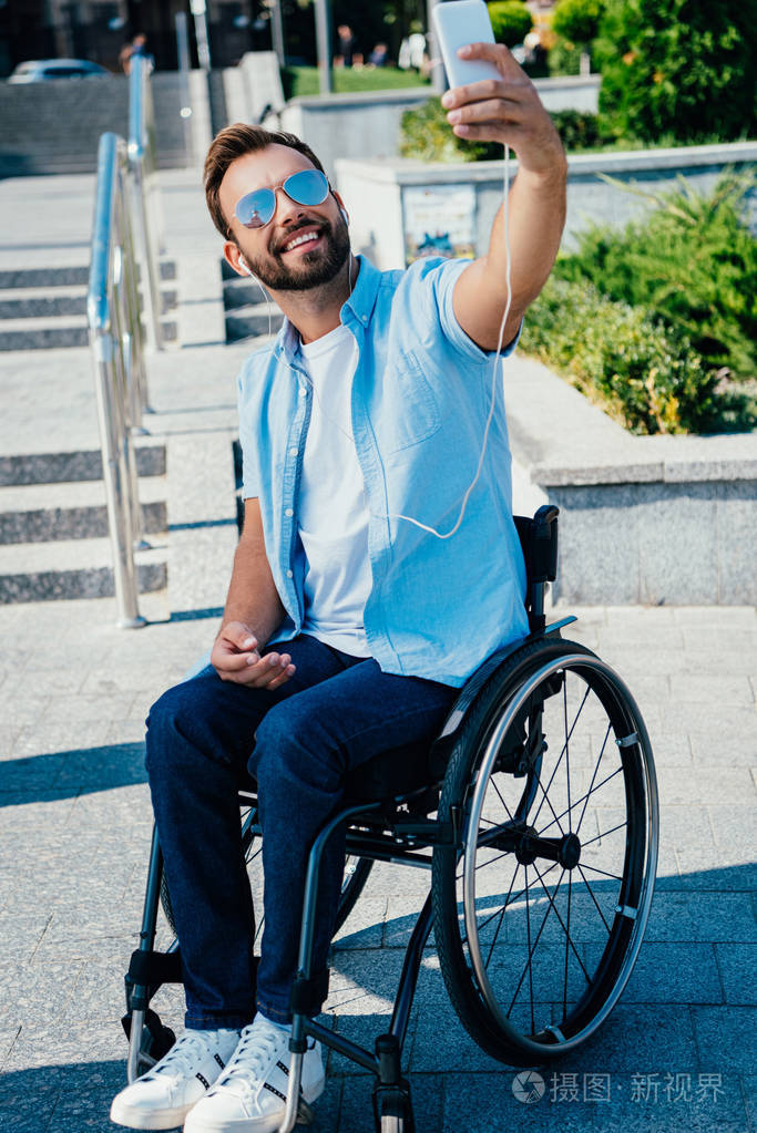 英俊的人在轮椅上自拍与智能手机和听音乐在街上照片-正版商用图片09