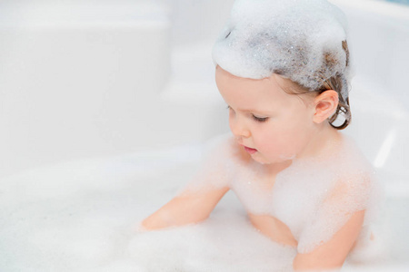 小女孩在浴缸里玩肥皂的乐趣在头上