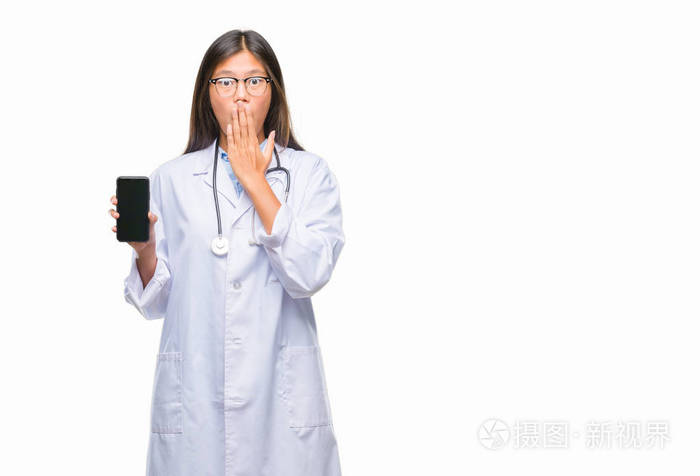年轻的亚洲医生妇女持有智能手机在孤立的背景下捂着嘴用手震惊的错误, 表达恐惧, 害怕沉默, 秘密概念
