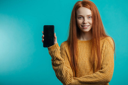 在蓝色天空手持智能手机的 redhaired 妇女的肖像