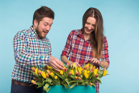 快乐的男人和女人花店举行的郁金香和笑蓝色背景的盒子