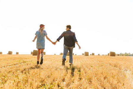 后视图的一对快乐的年轻夫妇一起走在麦田, 握着手