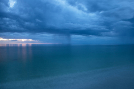 雨从乌云上倾泻而下, 在那不勒斯的海蛤湾海滩, 日落时分的佛罗里达