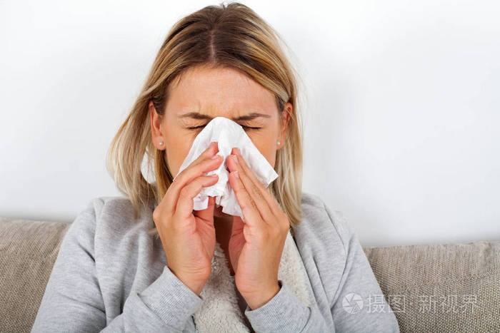 一个生病的年轻女士坐在沙发上, 吹她流鼻涕的图片照片-正版商用图片