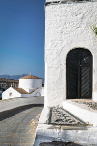 这是一个木门的图片, 这是一个白色的洗涤建筑物的入口, 在一个小教堂的背景下的希腊村庄